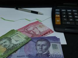 Chilean banknotes, pen and calculator on background with rising trend green line photo