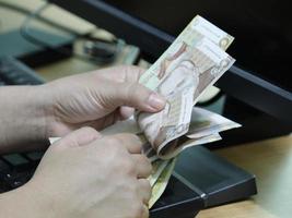 Manos de una mujer contando dinero peruano en un teclado de computadora foto