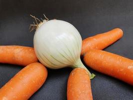 Trozos de verduras de zanahoria fresca y una cebolla blanca sobre la superficie negra, verduras frescas de origen natural para preparar comida vegetariana. foto
