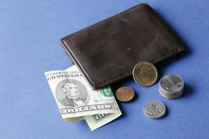 Billete de cinco dólares americanos, monedas y billetera de cuero marrón sobre fondo azul.