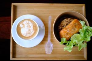 taza de café con latte art en forma de cisne y filete de salmón frito foto