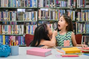 Two little happy cute girls making funny face and playing together in library at school as dental health check. Education and self learning wireless technology. People lifestyles and friendship photo