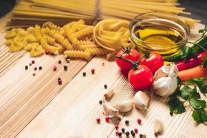 Tasty appetizing italian spaghetti pasta ingredients for kitchen cuisine with tomato, cheese parmesan, olive oil, fettuccine and basil on wooden brown table. Food Italian recipe homemade. Top view photo