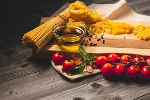 Tasty appetizing italian spaghetti pasta ingredients for kitchen cuisine with tomato, cheese parmesan, olive oil, fettuccine and basil on wooden brown table. Food Italian recipe homemade. Top view photo