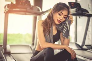 Woman sweats by towel during rest in fitness gym with fitness running equipment. Beauty and relax concept. Gym and fitness training theme photo
