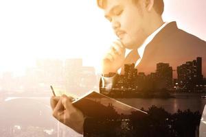 Businessman looking memo and Thinking for idea,Double exposure, panoramic view contemporary megalopolis background, orange sun light photo