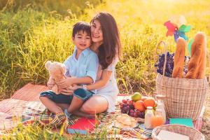 Beautiful Asian mother and son doing picnic and in Easter summer party on meadow near lake and mountain. Holiday and Vacation. People lifestyle and Happy family life concept. Thai person photo