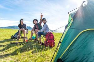 Group of hikers looking at attraction view point at meadow field with mountain and lake background. People and lifestyles concept. Hiking and Travel theme. Three people with backpack. Tent foreground photo