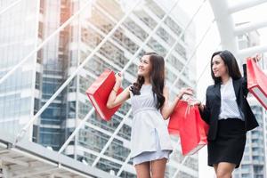 Two Asian Business women carrying red shopping bags with department store background in metropolis or city. Relax and Happiness of people lifestyle concept. Hobbies and leisure in vacation theme