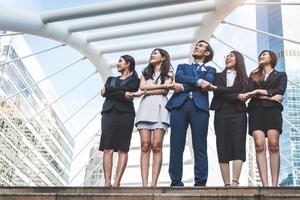 Portrait of successful group of business people looking up to sky as future. Happy businessmen and businesswomen team in satisfaction gesture. Successful group of people smiling in city background photo