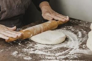 Female chef using rolling pin for preparing pizza dough photo