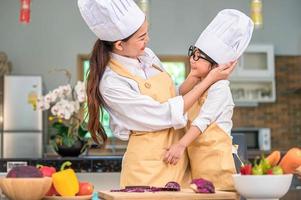 Happy cute little boy with eyeglasses looking beautiful Asian woman mother each other while prepare to cooking in kitchen at home. People lifestyles and Family. Homemade food and ingredients concept