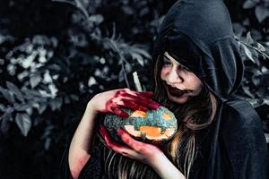 bruja demonio cuida de la calabaza en el bosque misterioso. concepto de fantasma y terror. tema del día de halloween. sangre roja en manos de bruja