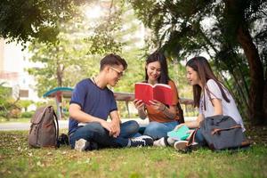 Group of Asian college student reading books and tutoring special class for exam on grass field at outdoors. Happiness and Education learning concept. Back to school concept. Teen and people theme photo