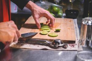 Closeup of professional bartender hand slicing lemon for making lemonade juice by knife in night club. Chef making drinks for guest in pub restaurant. Food and beverage concept photo