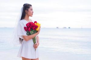 mujer asiática sosteniendo flores y esperando que alguien la haga feliz. concepto de mujer solitaria y soltera. concepto de tristeza y destino. tema de belleza y naturaleza. tema del océano y el mar. Encontrar el tema del alma gemela foto