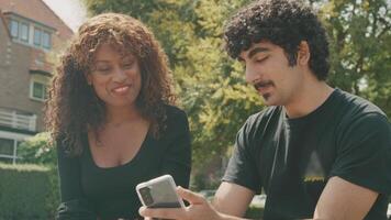 El hombre sostiene el teléfono inteligente y habla de él mientras está sentado con la mujer en el parque video