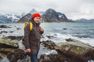 Fotógrafo viajero de pie sobre las rocas contra el fondo del mar y la montaña