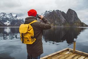 Hombre hablando por teléfono móvil en una mochila amarilla de pie sobre un fondo de una montaña y un lago foto