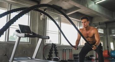 Young man working out with battle ropes at gym