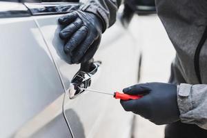 The thief uses a screwdriver to break into a car