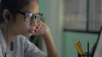 Girl in eyeglasses wears earphone watching lesson online from laptop. video