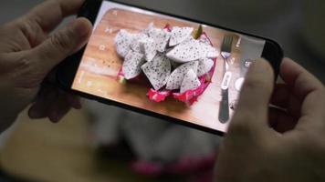 manos de mujer tomando fotografías de fruta del dragón preparada con smartphone. video