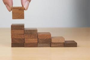 Mano arreglando el apilamiento de bloques de madera como escalera en la mesa de madera foto