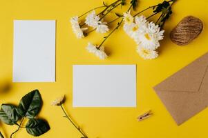 Se coloca una tarjeta en blanco con sobre y flor sobre fondo amarillo. foto