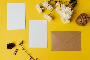 Se coloca una tarjeta en blanco con sobre y flor sobre fondo amarillo. foto