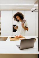 Black young woman making breakfast while using cellphone at kitchen