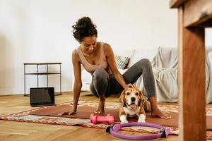 Joven negra sonriendo y acariciando a su perro durante la práctica del yoga foto