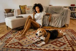 Black woman using cellphone while sitting on floor with her dog photo