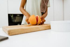Black young woman cutting grapefruit while cooking at kitchen
