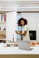 Joven negra abriendo el congelador mientras prepara el desayuno en la cocina foto