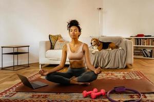 Black young woman meditating during yoga practice with her dog photo