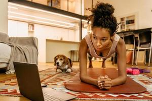 Black young woman using laptop while doing exercise during workout photo