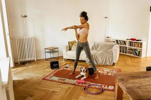 Black young woman doing stretching exercise during yoga practice with her dog photo