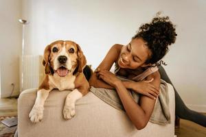 Black young woman laughing while resting with her dog on sofa photo