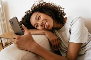 Black young woman using mobile phone while resting on sofa photo