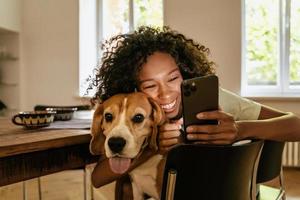 Joven negra abrazando con su perro mientras usa el teléfono móvil foto