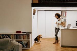 Black young woman having breakfast while looking at her dog in kitchen