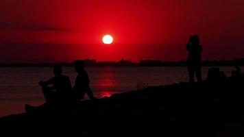 silhouetten van mensen die bij zonsondergang naar de zee kijken op het strand video