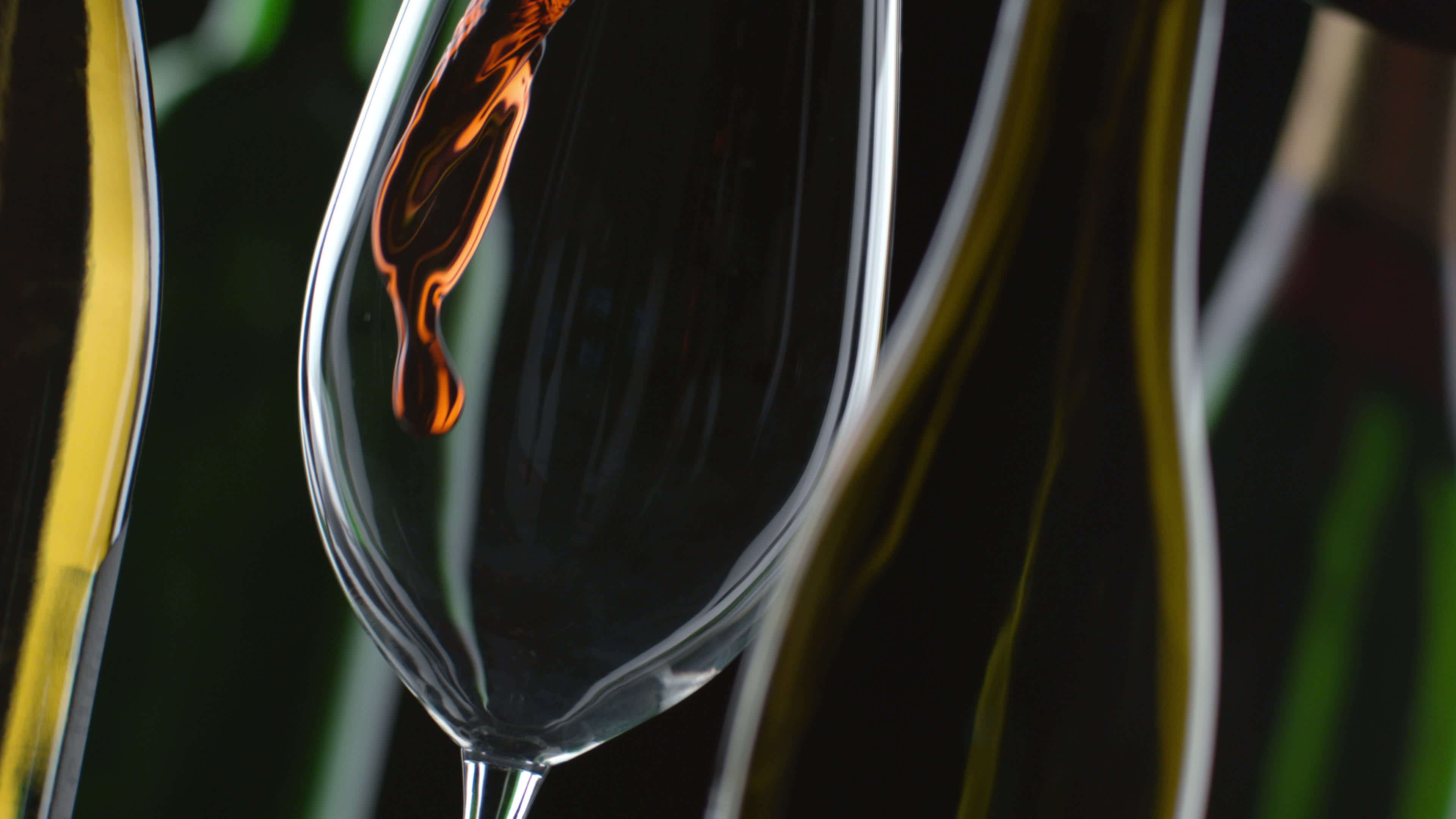 Slow motion shot of red wine pouring with bottles and black background