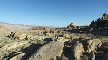 Toma aérea de un mochilero joven parado sobre una roca con su perro en una cordillera del desierto. video