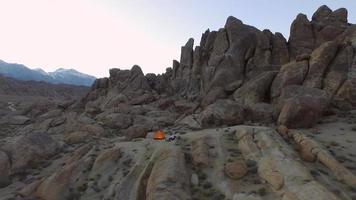 Toma aérea de un mochilero joven acampando con su perro en un desierto montañoso.