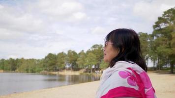 mulher idosa asiática de óculos em pé na praia para ver uma vista maravilhosa do mar e olhando para o céu. tendo um tempo maravilhoso e muita felicidade. permanecendo saudável video