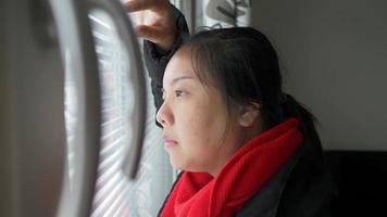 mulher asiática triste caminhando para a janela e olhando para fora pela janela, vendo a bela vista lá fora, ficando entediada em casa, quarentena e fique segura durante 19 video