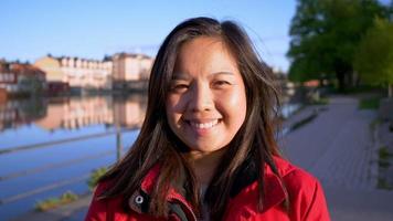 Close up front view of Asian woman smiling by river in the evening. Going for a walk, getting some fresh air and staying healthy. Happy face and happy life concept. River background video