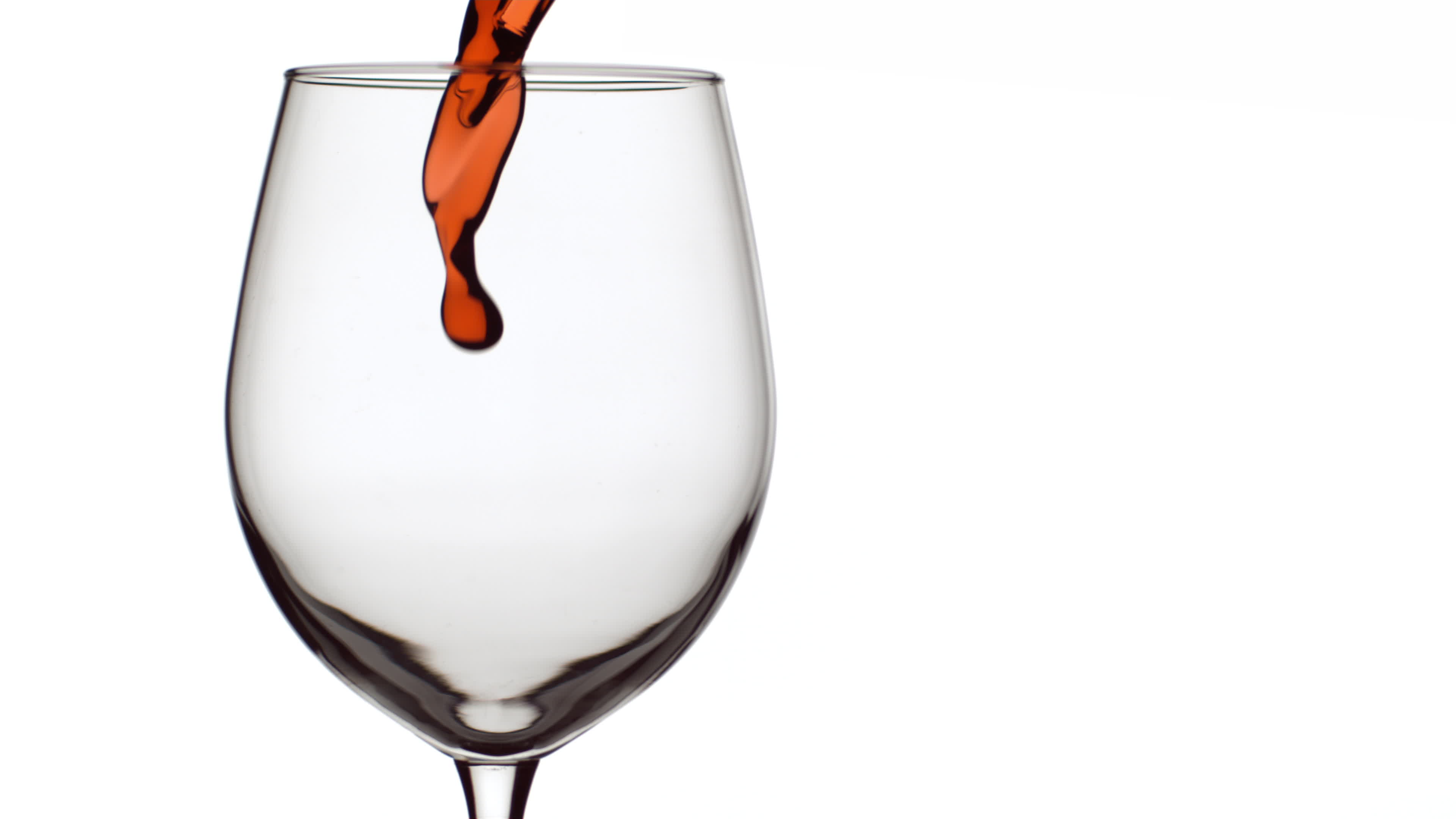 Slow motion shot of red wine pouring into glass on white background